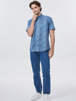Man wearing a blue patterned shirt and jeans on a white background. Leo Chevalier 