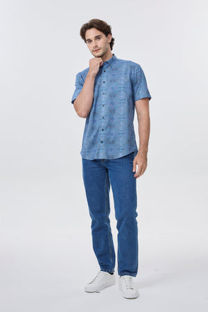 Man wearing a blue patterned shirt and jeans on a white background. Leo Chevalier 